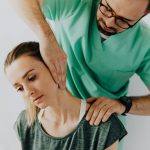 Confident doctor wearing uniform and eyeglasses gently doing therapeutic massage on calm female patients neck and stretching stiff neck muscles