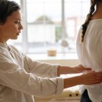 A physiotherapist performs a back alignment therapy on a patient indoors.